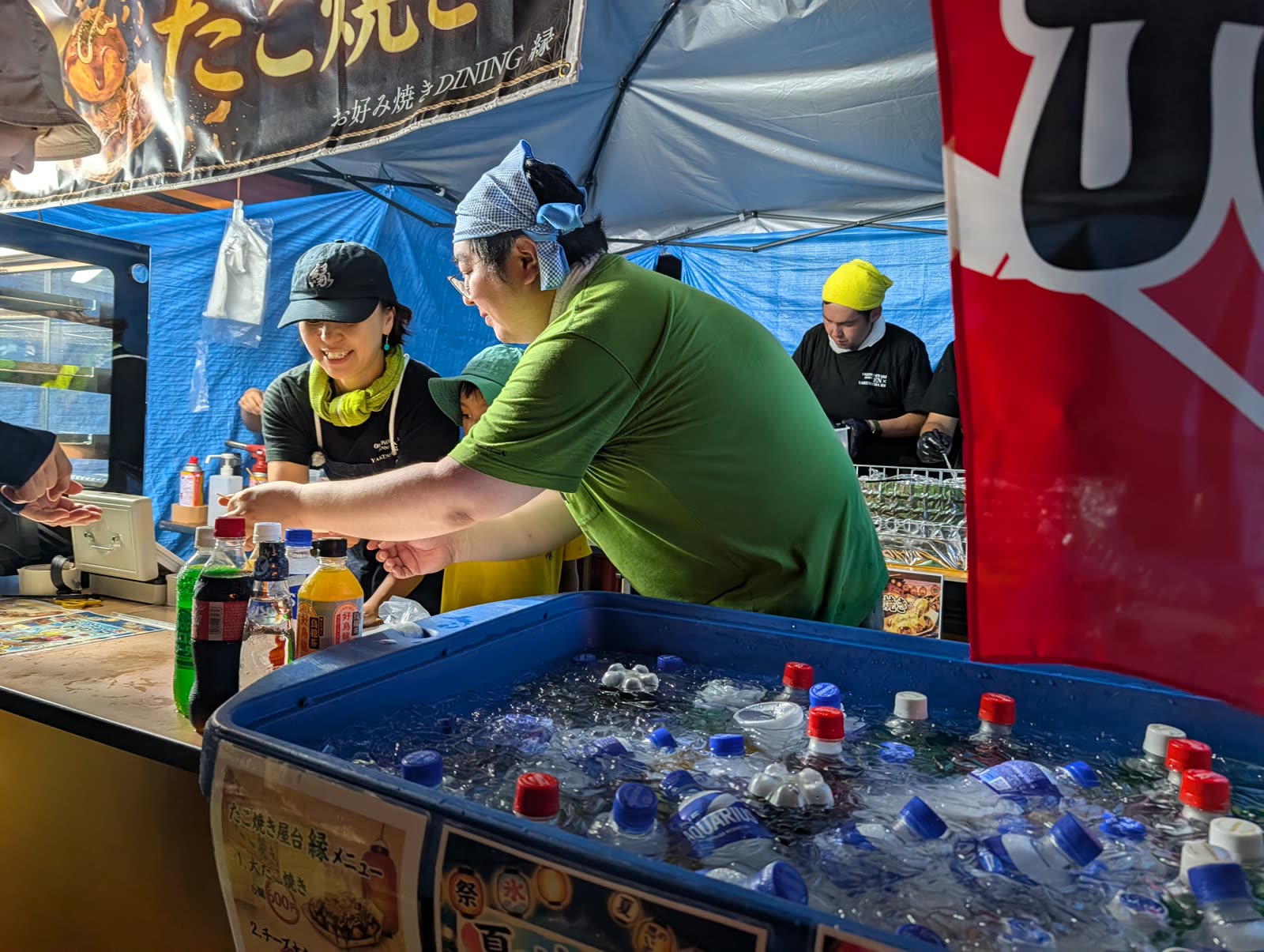 ご神山祭り当日の縁の屋台。カウンター越しに接客するスタッフと、氷水で冷やしたドリンク